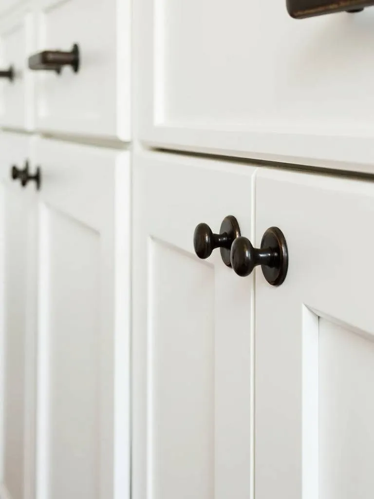 Detail shot of farmhouse kitchen hardware featuring oil-rubbed bronze bin pulls and knobs, demonstrating the impact of thoughtful hardware selection.