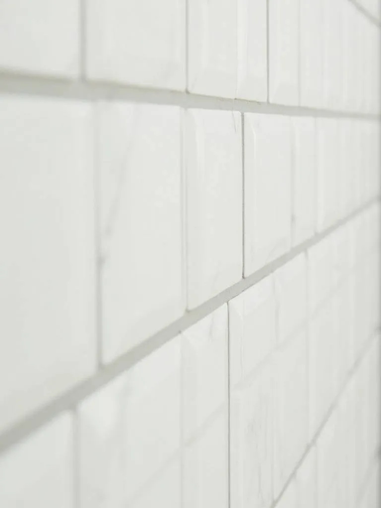 “Close-up of a bathroom wall tiled with vertically stacked white rectangular tiles, creating an illusion of height.”