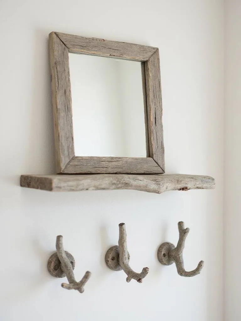 Bathroom accents made from driftwood, such as a mirror frame, shelf, or towel hooks, adding weathered, coastal texture.