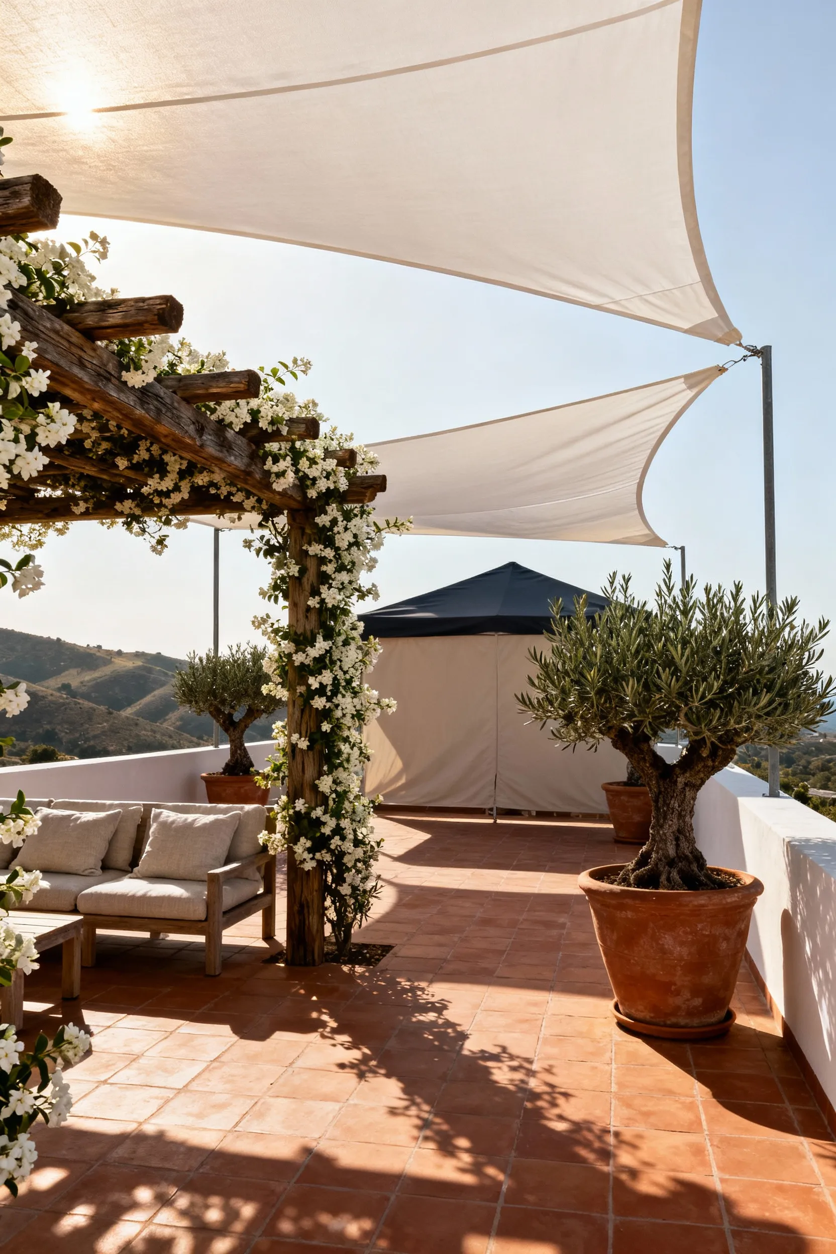 Elevated Mediterranean deck showing 'shade progression' with a rustic pergola, jasmine vines, retractable sail shades, large olive tree planters, and terra cotta tiles, featuring dappled light and cool shadows.