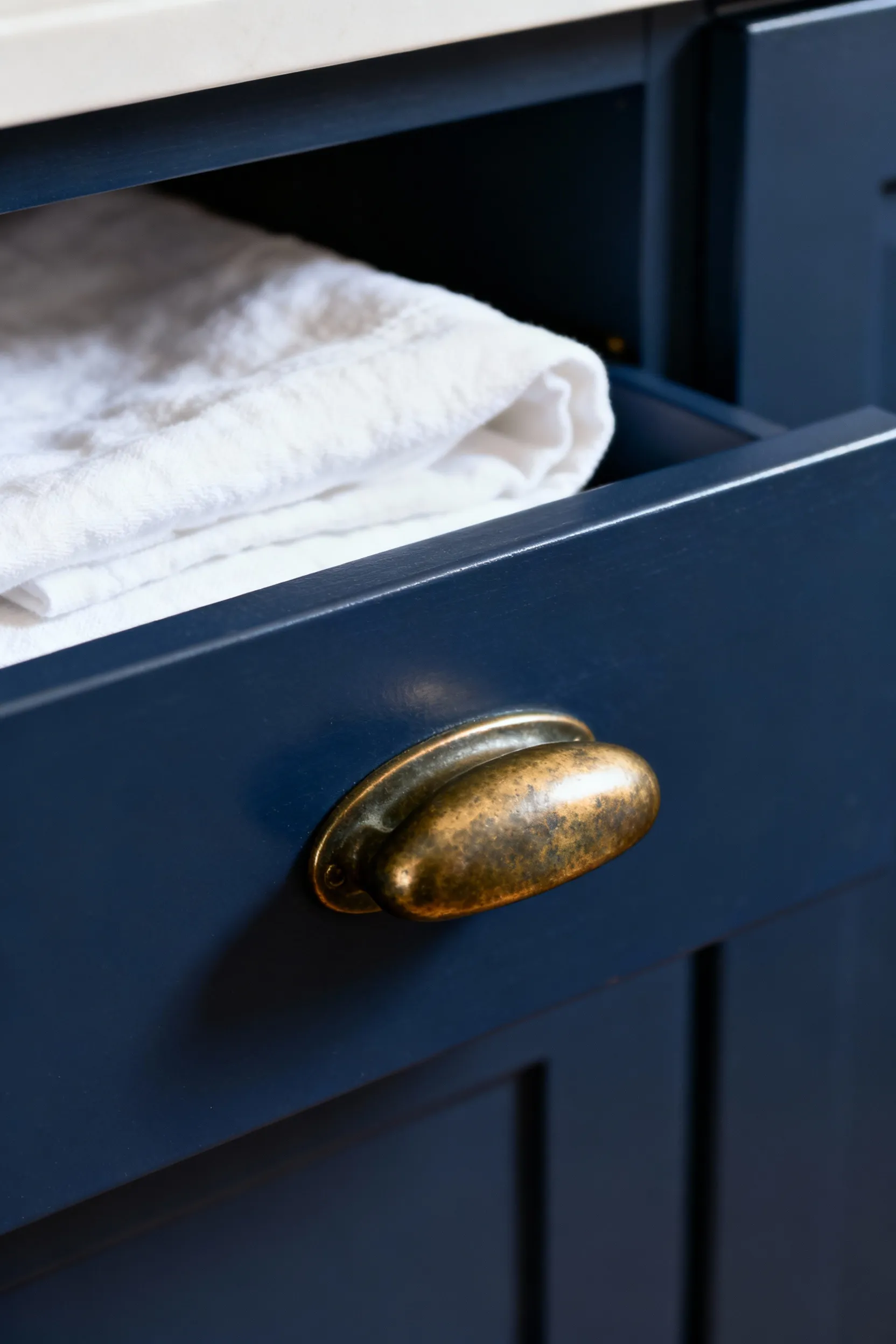 Close-up portrait view of a finely crafted, solid forged brass drawer pull with a patinated finish on a luxury laundry cabinet, highlighting tactile elegance.