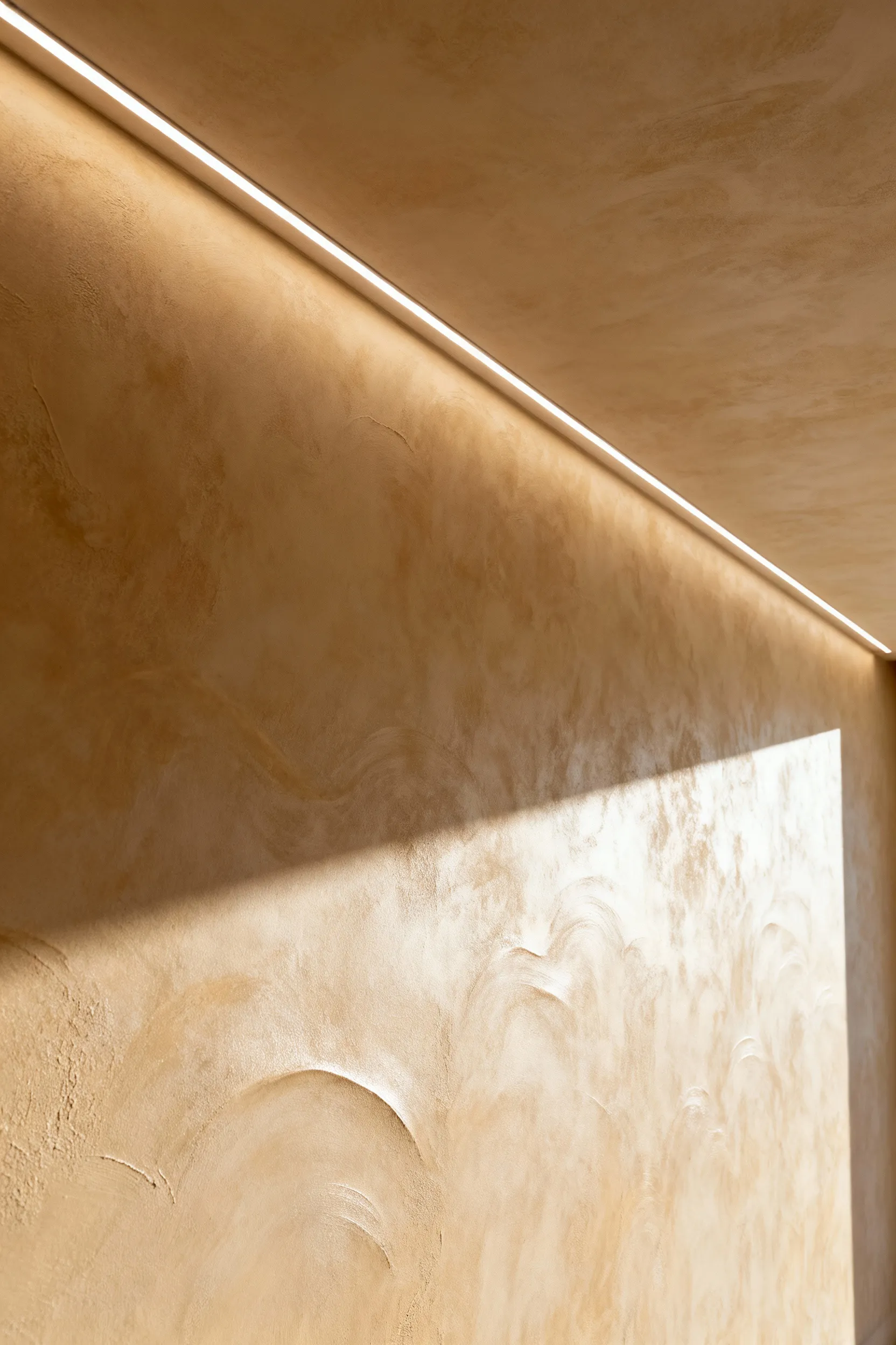 Luxurious living room wall featuring warm beige Venetian plaster with grazing integrated lighting highlighting its sophisticated texture and depth.